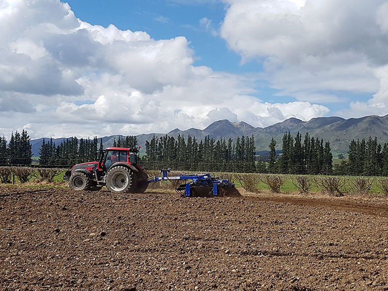 Red tractor pulling Walter Watson rollers across field for spring cultivation. NC Equipment North Canterbury New Zealand